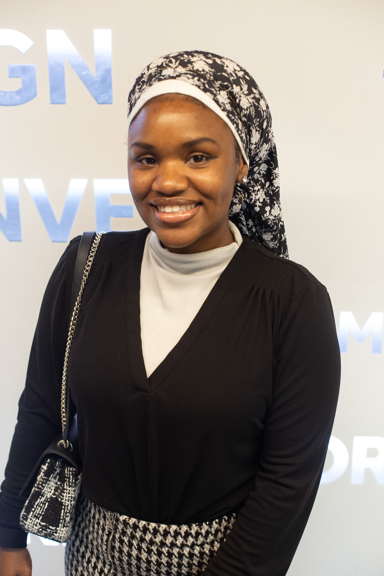 Portrait — smiling in a floral headwrap, houndstooth skirt and tweed bag