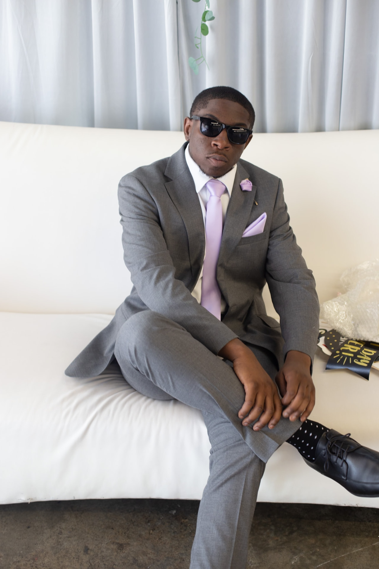 Wedding — groomsman in shades seated on the white sofa, polka-dot socks out