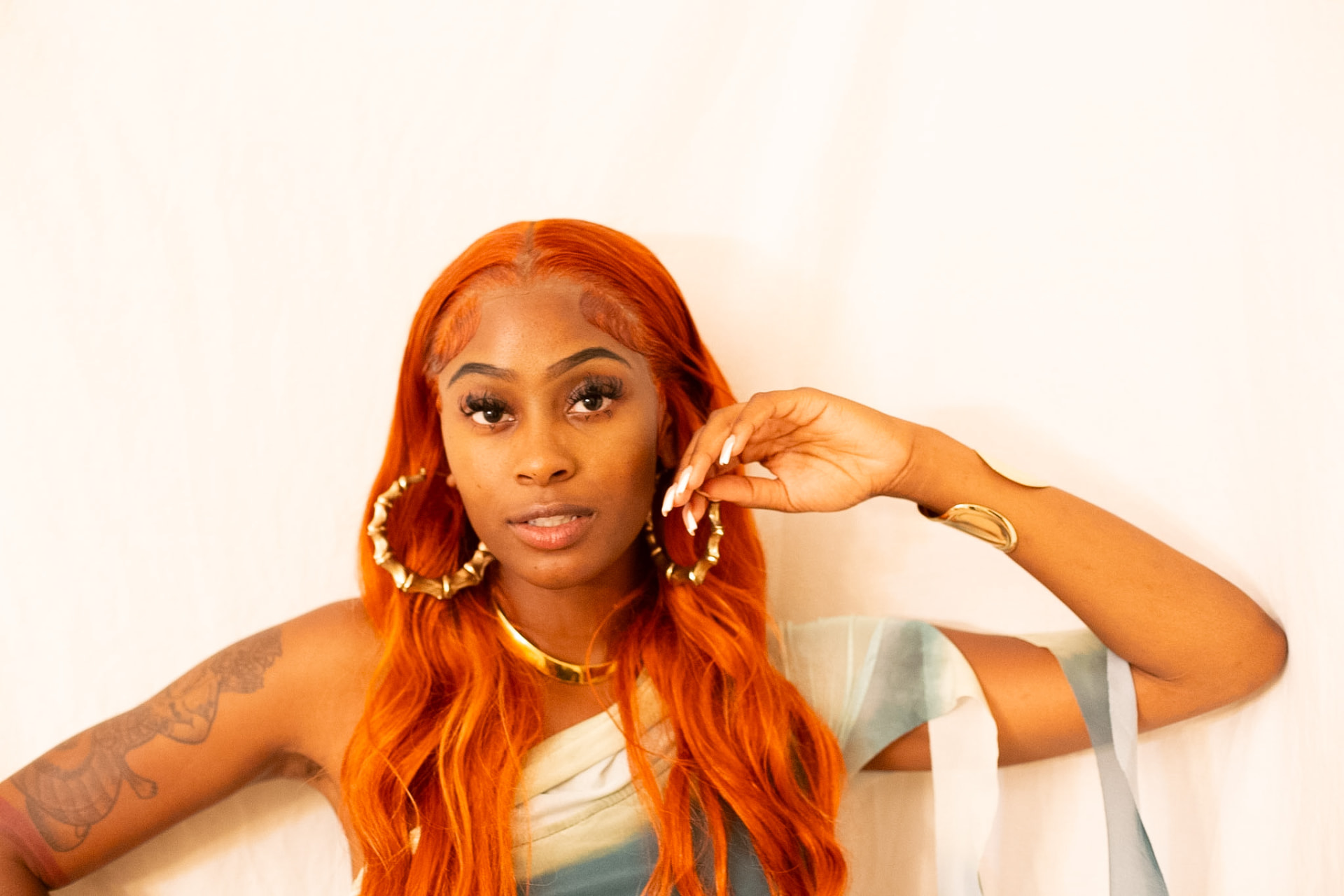 Model portrait — copper hair, bamboo hoops and gold against the sheets