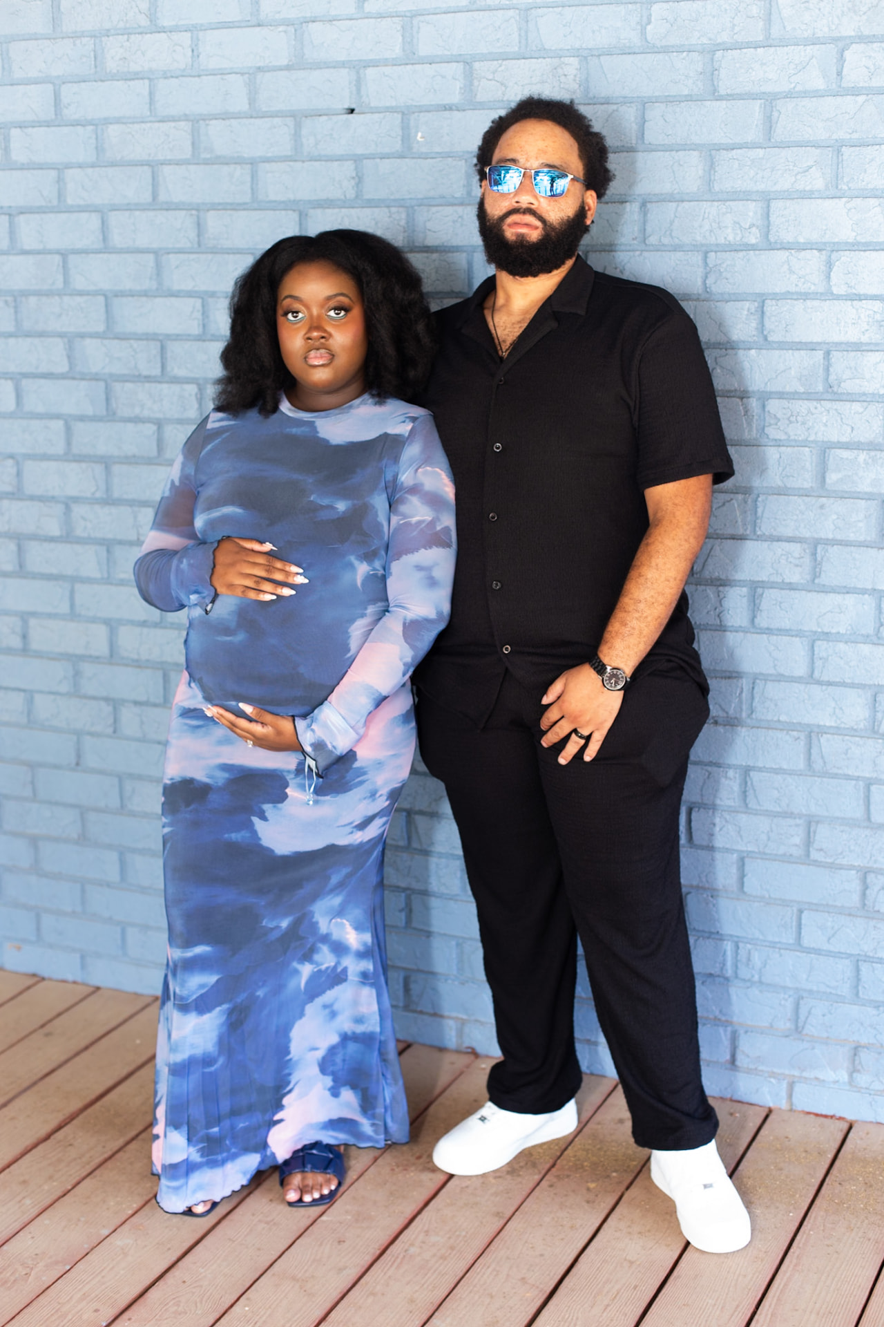 Maternity event session — couple against the blue brick wall